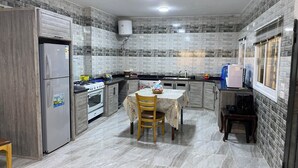 Eine Küche mit Kühlschrank, Herd, Backofen und einem Esstisch mit Stühlen.