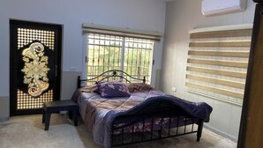 Ein Schlafzimmer mit Bett, einer Bank, einem Fenster mit Aussicht und einer Tür mit dekorativem Muster.