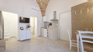 A modern kitchen with a TV, a dining area with a table and chairs, and a stone archway. - Dimor Monolocale Deluxe (Casarano)