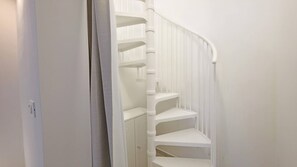 Una escalera en espiral blanca con barandilla, que lleva a una plataforma con una puerta.
