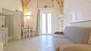 A room with a stone arch, a dining area with a table and chairs, a sofa, and a white cabinet. - Dimor Monolocale Deluxe (Casarano)