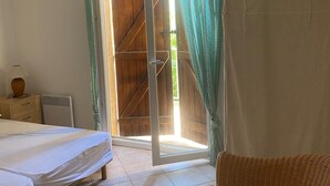 A room with a bed, a wicker chair, a wooden door, and a radiator. - Villa Spacieuse Avec Piscine Priv e 150 m de la Plage Calvi Centre (Calvi)
