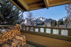 A wooden deck with a railing, a stack of firewood, and a view of snow-capped mountains.