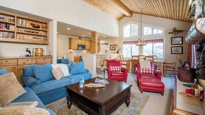 Ein geräumiges Wohnzimmer mit einem blauen Sofa, einem roten Ledersessel, einem Couchtisch aus Holz und einer Küche im Hintergrund.