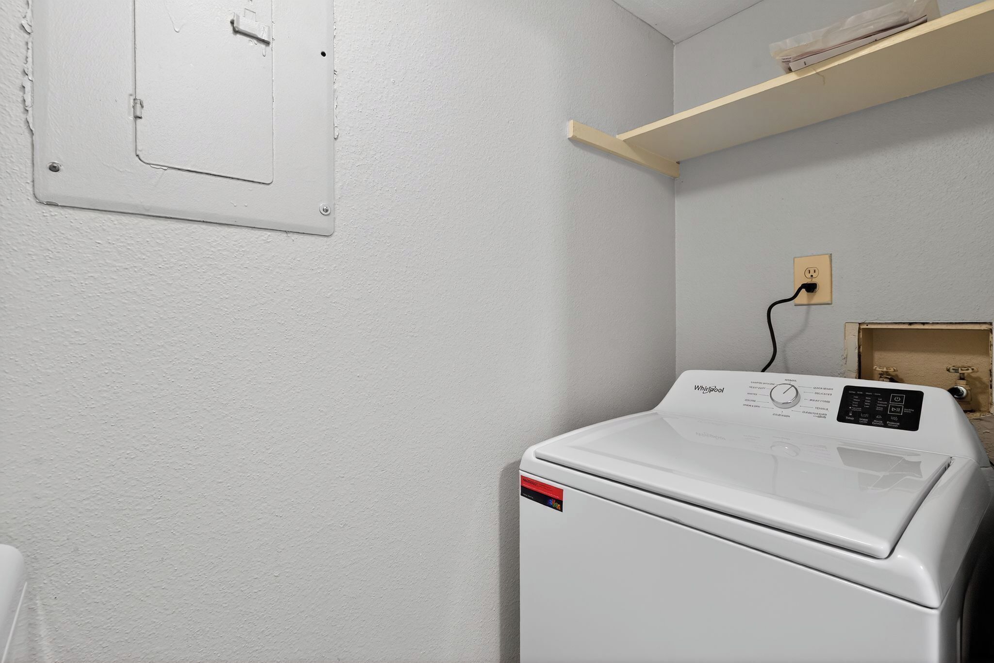 Eine kompakte, weiße Whirlpool Waschmaschine mit Bedienfeld, einer Steckdose und einem Lichtschalter an der Wand.