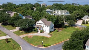 A residential area with houses, a well-maintained lawn, and a body of water in the background. - Sweet Caroline's: Flexible Stays, Dog-friendly, Close to Beach (Corolla)