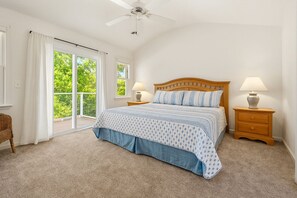 A bedroom with a bed, two bedside tables, a ceiling fan, and a view of greenery through the window. - Sweet Caroline's: Flexible Stays, Dog-friendly, Close to Beach (Corolla)