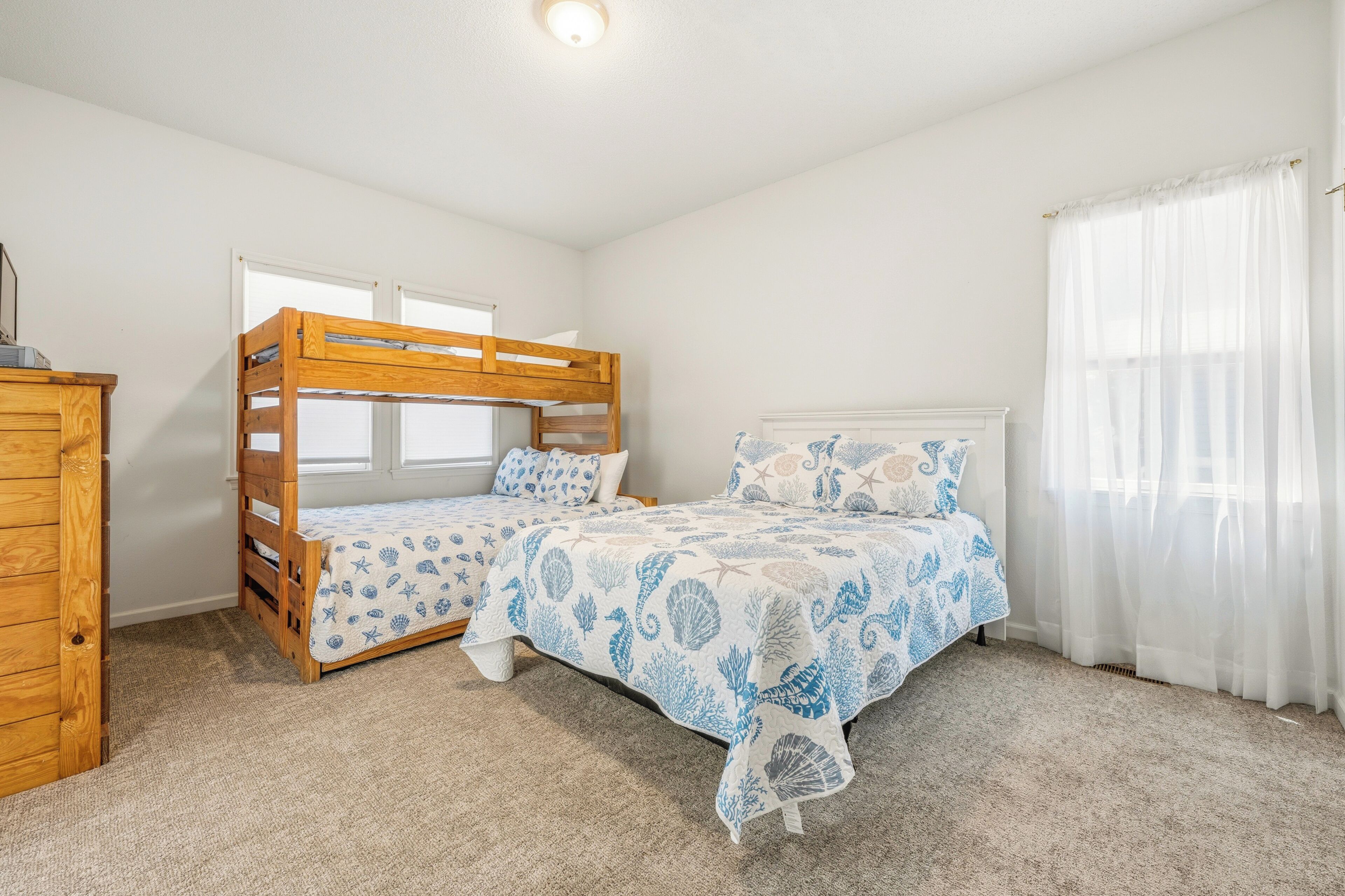 Une chambre avec des lits superposés, une commode en bois et une fenêtre ornée de rideaux légers.