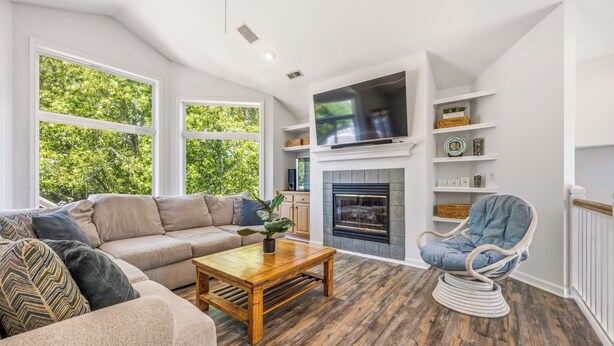 A living room with a sofa, armchair, coffee table, fireplace, TV, and large windows. - Sweet Caroline's: Flexible Stays, Dog-friendly, Close to Beach (Corolla)