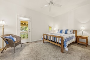 A bedroom with a bed, a chair, a nightstand, a ceiling fan, and a door. - Sweet Caroline's: Flexible Stays, Dog-friendly, Close to Beach (Corolla)