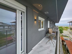 Ein Balkon mit Tisch und Stühlen, ein Fenster und Blick aufs Meer.
