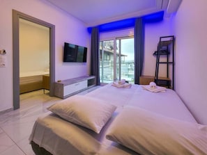 A hotel room with a bed, a TV, a bench, and a view of the outside. - 13 - DELFINI Suites by SDR (Paralia)