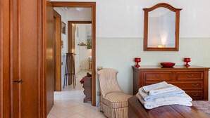 A room with a wooden door, a chair, a table with a towel, a dresser, and a mirror.