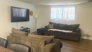 A living room with a flat-screen TV, a sofa, a coffee table, and a dining area with chairs.