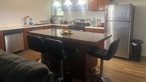 A modern kitchen with a central island, bar stools, stainless steel appliances, and pendant lighting.