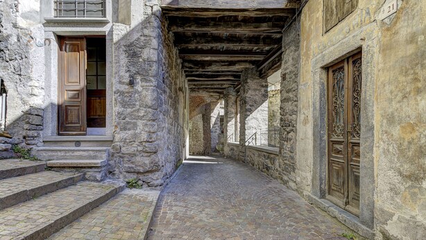 Une ruelle pavée bordée de bâtiments en pierre, de portes en bois et d’un escalier en pierre.
