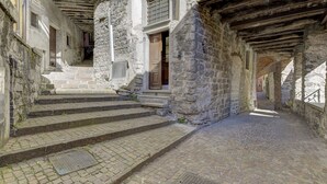 Un bâtiment en pierre avec un escalier menant à une porte en bois, un sol pavé de pierres et une grille en métal.