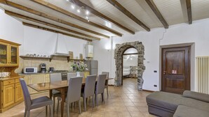 Une cuisine avec une table à manger, des chaises et une arche en pierre qui mène à une autre pièce.
