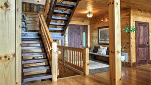 Un escalier en bois avec une rampe, une porte en bois avec une fenêtre et un canapé avec des coussins.