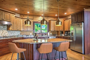 Una cocina con gabinetes de madera, un refrigerador de acero inoxidable e una isla central con taburetes de bar.