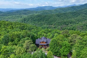 A house surrounded by dense forest, with a prominent roof and a front porch.