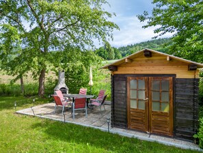 A rustic cabin with a fireplace, outdoor seating, and a door with frosted glass panels.