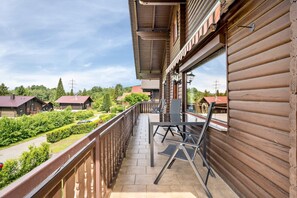 Een balkon met een tafel en stoelen, uitzicht op een weg en groen, en een gebouw met houten bekleding.