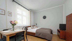 A bedroom with a bed, a TV, a wooden desk with chairs, and a window with curtains. - Functional Studio in the Center | Close to the Market | Smart TV (Wrocław)