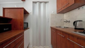 A kitchen with wooden cabinets, a bread box, a microwave, a kettle, and a sink. - Functional Studio in the Center | Close to the Market | Smart TV (Wrocław)