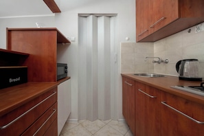 A kitchen with wooden cabinets, a bread box, a microwave, a kettle, and a sink. - Functional Studio in the Center | Close to the Market | Smart TV (Wrocław)
