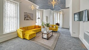 Een woonkamer met een gele bank, een salontafel en een aan de muur bevestigde televisie.