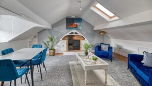 Een loft met een woonruimte, een eethoek, blauw meubilair, een open haard en een dakraam.