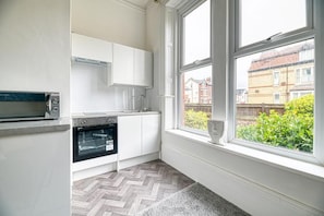 Une cuisine avec des armoires blanches, un four encastré et une fenêtre donnant sur un quartier résidentiel.