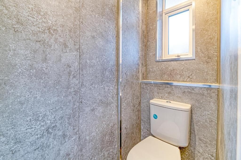 A bathroom with a toilet, a window, and a textured wall.