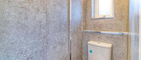 A bathroom with a toilet, a window, and a textured wall.