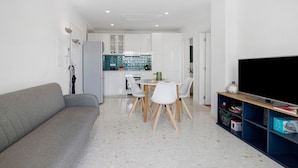 En moderne stue med sofa, spisebord, stole, fjernsyn og et køkken.