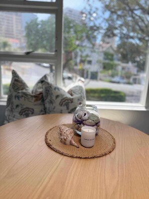 A round wooden table with a woven placemat, a glass jar with decorative items, a candle labeled 'ADRIAN WILLIAM,' and a seashell. - Chic Waterfront Stay with Prime Sydney Access (Lavender Bay)