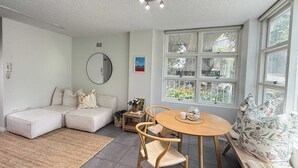 A living room with a sofa, a round table, and a window with a view of greenery. - Chic Waterfront Stay with Prime Sydney Access (Lavender Bay)