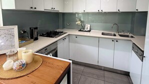 A modern kitchen with white cabinets, a wooden table, a coffee maker, and a sink. - Chic Waterfront Stay with Prime Sydney Access (Lavender Bay)