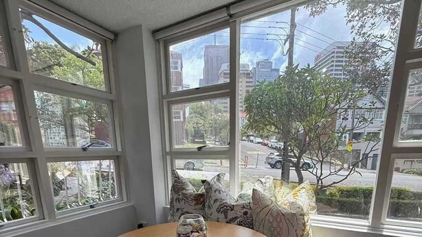 A round wooden table with two chairs, a glass vase with flowers, and a candle on a woven placemat. - Chic Waterfront Stay with Prime Sydney Access (Lavender Bay)