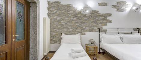 Un dormitorio con pared de piedra, puerta de madera, cama con ropa blanca y cabecera de mimbre.