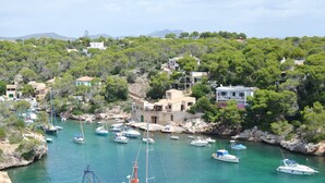 Un village côtier où des bateaux sont amarrés dans une marina, entouré d’une végétation luxuriante et de bâtiments à l’architecture méditerranéenne.