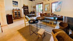 Un salon spacieux avec un plafond haut, des poutres apparentes, un lustre, un canapé, une table basse et une cheminée.