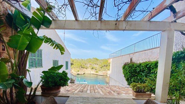 Une terrasse avec une table et des chaises, des plantes en pot, une vue sur une piscine et un bâtiment aux volets verts.