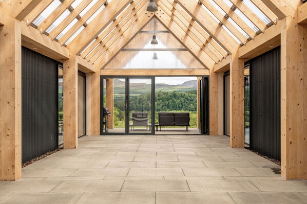 A spacious room with a high ceiling, large windows, and a view of a green landscape.