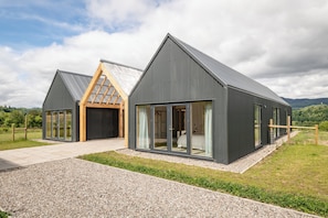 A modern building with large windows, a sloped roof, and a gravel driveway.
