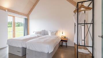 A bedroom with two beds, a wooden ceiling, a window with a view, and a hanging clothes rack.