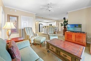 A living room with a sofa, armchairs, a coffee table, a TV, and a ceiling fan. - Royale Palms 1606 3 Br Oceanview in Kingston, Pool (Myrtle Beach)