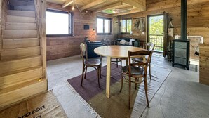 L’intérieur d’un chalet en bois comprend un coin repas, un canapé, une cheminée et une fenêtre donnant sur un paysage verdoyant.