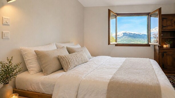 Une chambre à coucher avec un lit, une lampe de chevet, une fenêtre donnant sur la montagne et une table de chevet avec une bougie.